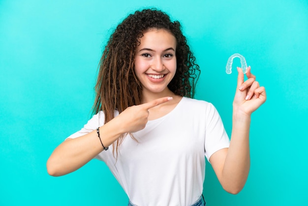 Young arab woman holding invisible braces isolated on blue background and pointing it