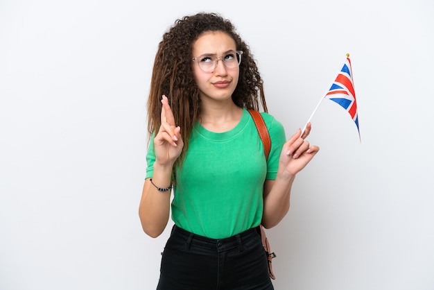 Young Arab woman holding an United Kingdom flag isolated on white background with fingers crossing and wishing the best