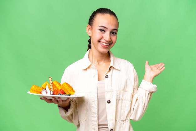 Young Arab woman holding waffles over isolated background extending hands to the side for inviting to come