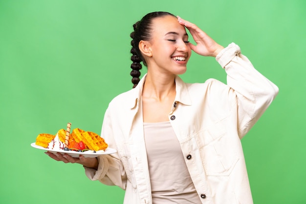 Young Arab woman holding waffles over isolated background smiling a lot