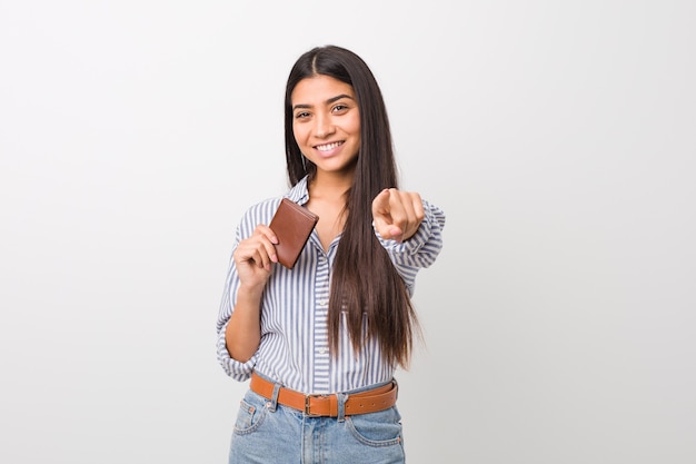 Young arab woman holding a wallet cheerful smiles pointing to front.