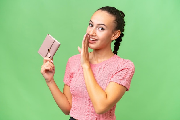 Young Arab woman holding a wallet over isolated background whispering something