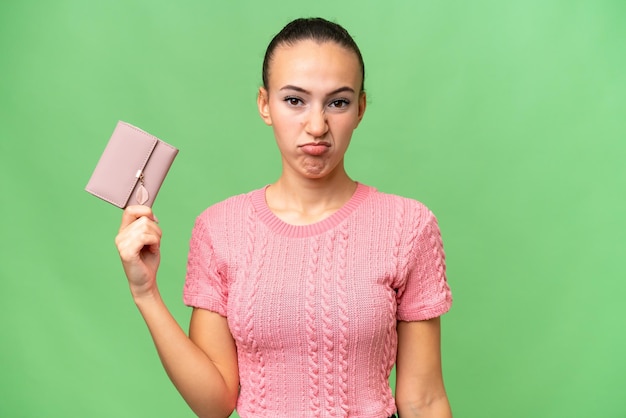 Young Arab woman holding a wallet over isolated background with sad expression