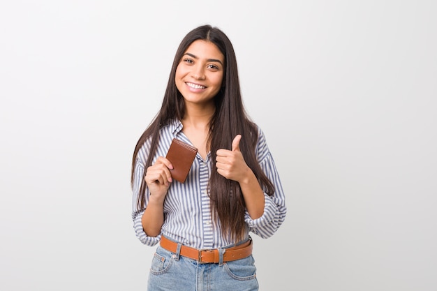 Young arab woman holding a wallet smiling and raising thumb up