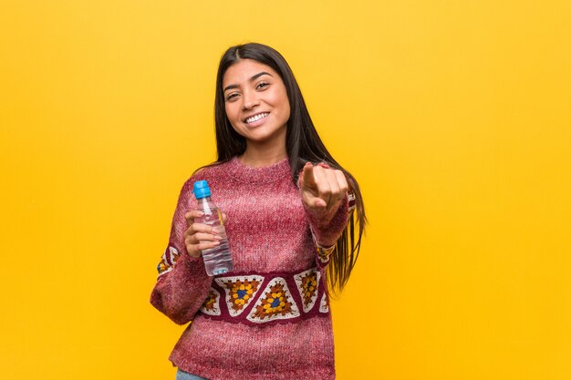 Young arab woman holding a water bottle cheerful smiles pointing to front.