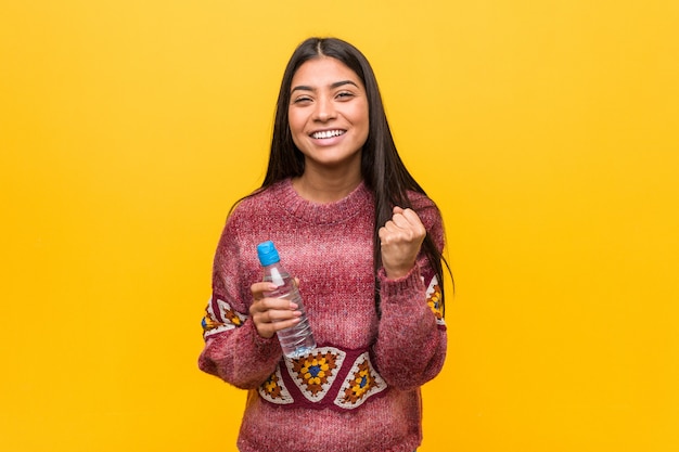 Young arab woman holding a water bottle cheering carefree and excited. Victory concept.