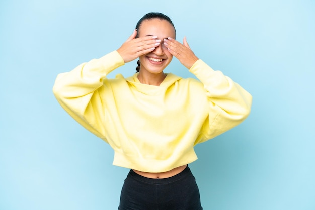 Young Arab woman isolated on blue background covering eyes by hands and smiling