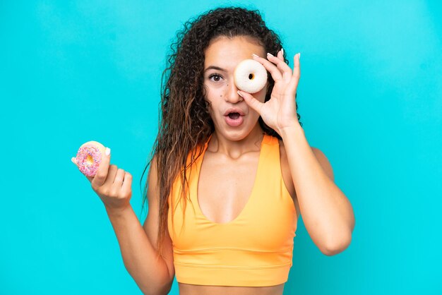 Young Arab woman isolated on blue background holding a donut in an eye