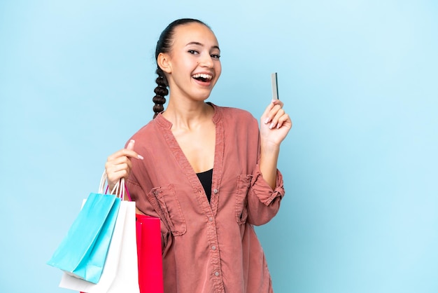 Young Arab woman isolated on blue background holding shopping bags and a credit card