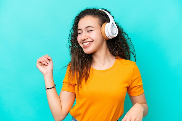 Young Arab woman isolated on blue background listening music and dancing