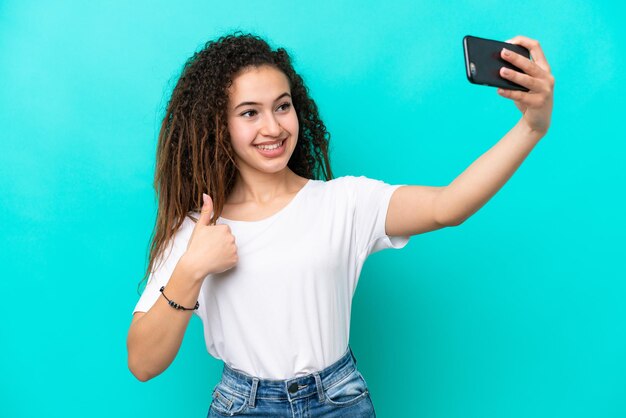 携帯電話でセルフィーを作る青色の背景に分離された若いアラブ女性