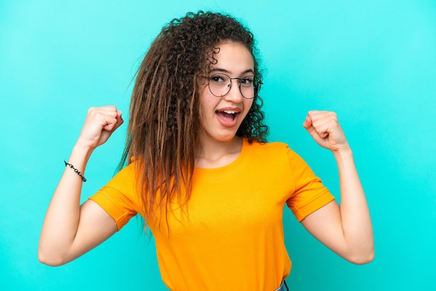 Young Arab woman isolated on blue background With glasses and celebrating a victory