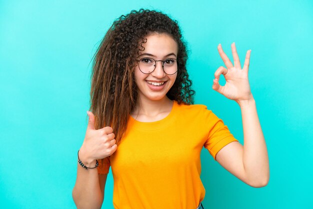 Foto giovane donna araba isolata su sfondo blu con gli occhiali e facendo segno ok