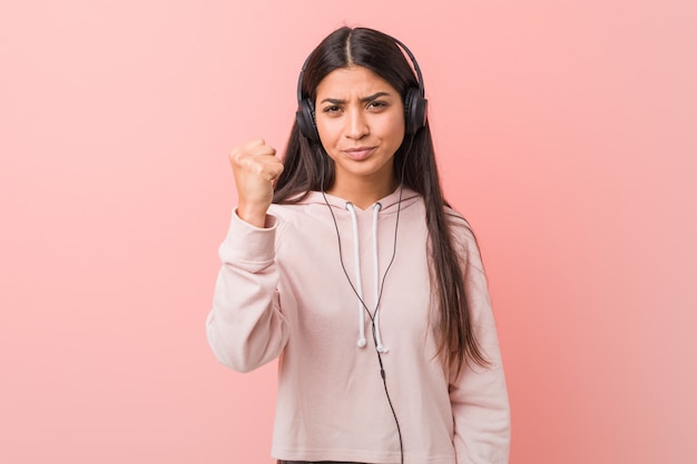 Young arab woman listening to music showing fist to camera, aggressive facial expression.