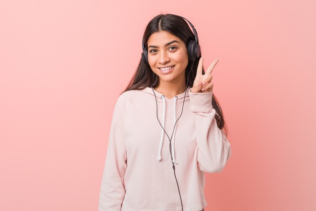 Young arab woman listening to music showing victory sign and smiling broadly.