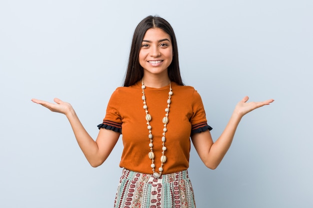 Young arab woman makes scale with arms, feels happy and confident.