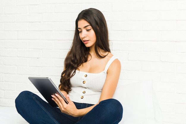 Young arab woman sitting on the bed using a tablet