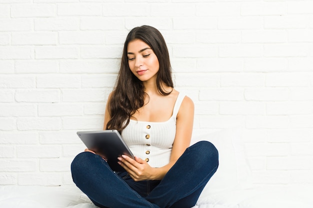 Young arab woman sitting on the bed using a tablet