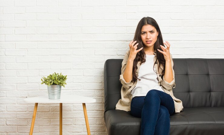 Photo young arab woman sitting on the sofa upset screaming with tense hands.