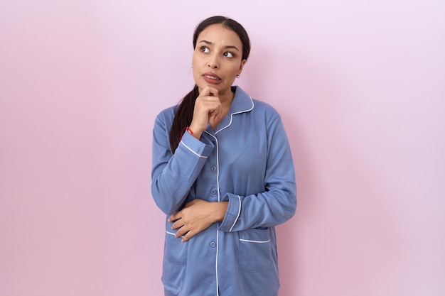 Young arab woman wearing blue pajama thinking worried about a question, concerned and nervous with hand on chin