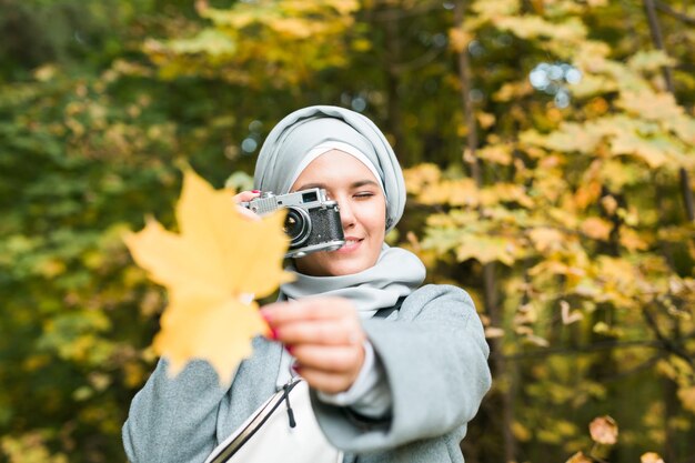 公園で現代のイスラム教徒の少女のスマートフォンで写真を撮るヒジャーブのヘッドスカーフを身に着けている若いアラブの女性