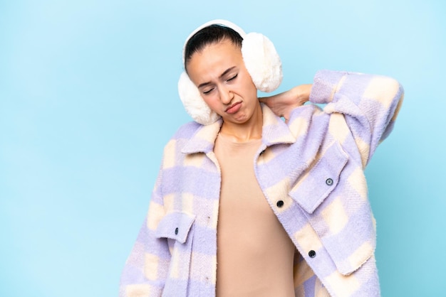 Young Arab woman wearing winter muffs isolated on blue background with neckache