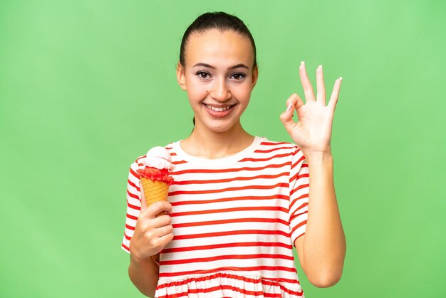 Young Arab woman with a cornet ice cream over isolated background showing ok sign with fingers