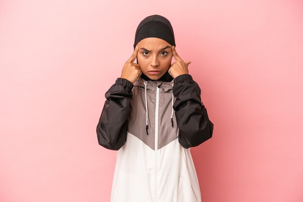 Young Arab woman with sport burqa isolated on pink background focused on a task, keeping forefingers pointing head.