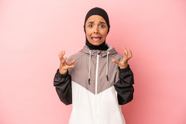 Young Arab woman with sport burqa isolated on pink background screaming with rage