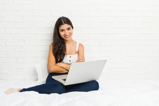 Young arab woman working with her laptop on the bed laughing and having fun.