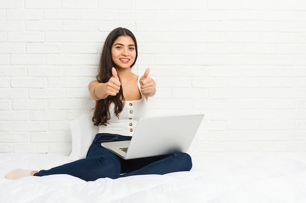 Young arab woman working with her laptop on the bed with thumbs ups