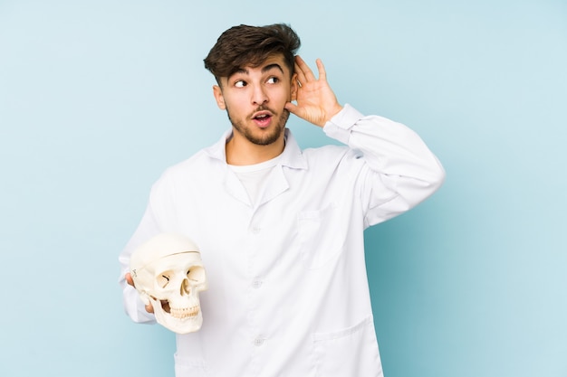 Young arabian doctor man holding a skull trying to listening a gossip.