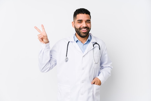 Young arabian doctor man joyful and carefree showing a peace symbol with fingers.