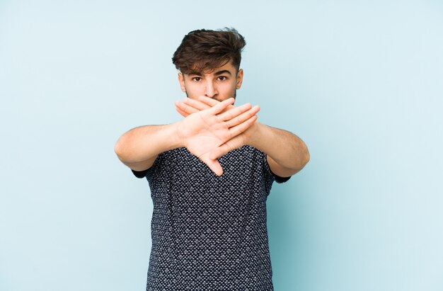 Young arabian man on a blue wall doing a denial gesture