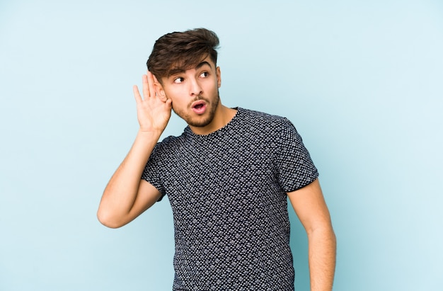 Young arabian man on a blue wall trying to listening a gossip.