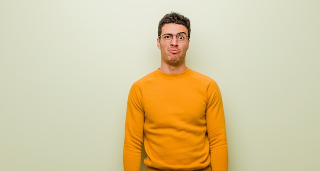 Young arabian man feeling sad and stressed, upset because of a bad surprise, with a negative, anxious look against flat wall