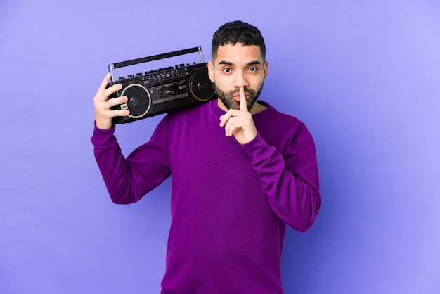 Young arabian man holding a radio cassette isolated young arabian man listening music keeping a secret or asking for silence