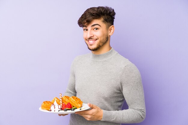 Young arabian man holding a waffle isolated laughing and having fun.