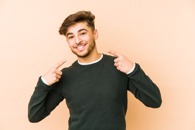 Photo young arabian man isolated on a beige wall smiles, pointing fingers at mouth.