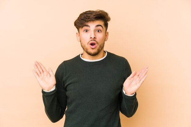 Young arabian man isolated on a beige wall surprised and shocked.