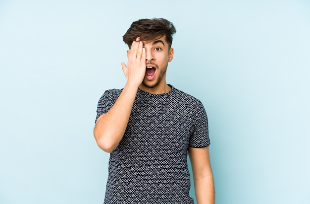 Young arabian man isolated on blue having fun covering half of face with palm.