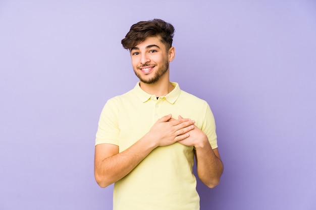 Young arabian man isolated on a purple has friendly expression, pressing palm to chest