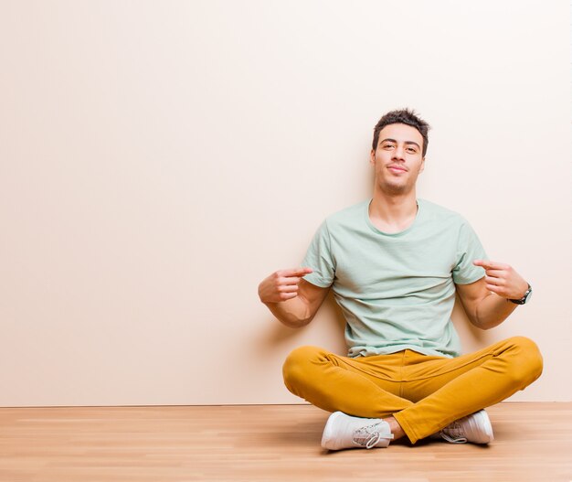 Photo young arabian man looking proud, arrogant, happy, surprised and satisfied, pointing to self, feeling like a winner sitting on the floor