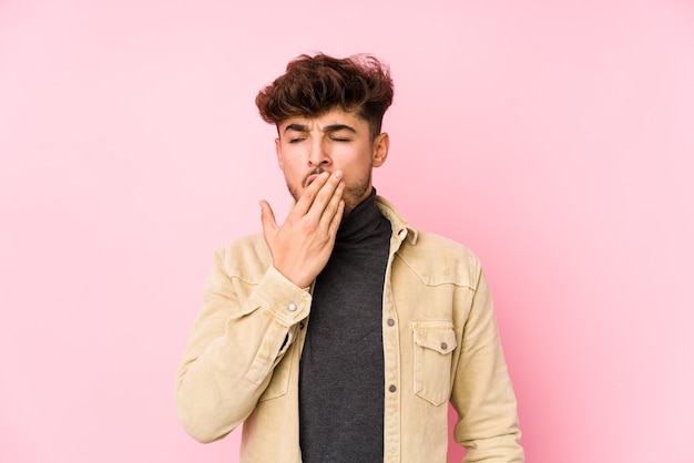 Young arabian man posing in a wall isolated yawning showing a tired gesture covering mouth with hand.