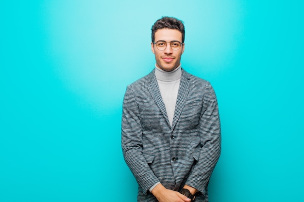 Young arabian man smiling positively and confidently, looking satisfied, friendly and happy against blue wall