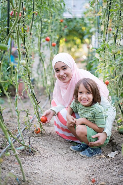 Young Arabian Muslim girl with little child working in greenhouse harvesting