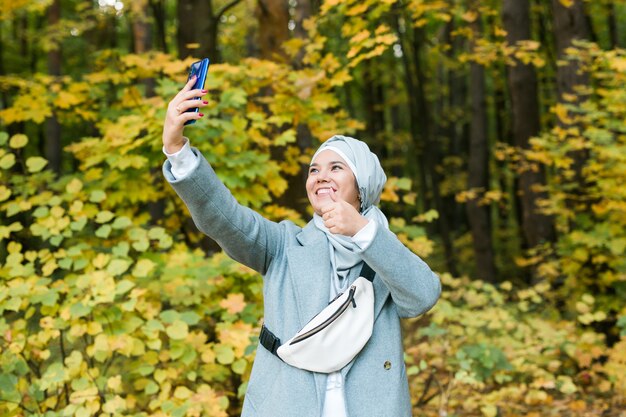 Young arabian muslim woman in hijab clothes doing selfie shot on mobile phone in park. People religious lifestyle concept. Copy space.