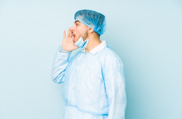 Young arabian surgeon man isolated against on a blue shouting and holding palm near opened mouth.