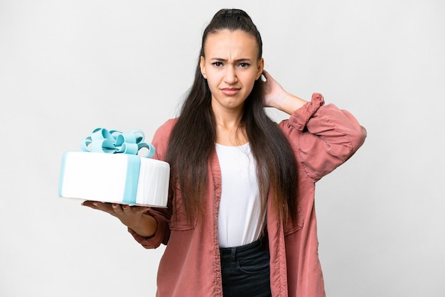 Giovane donna araba che tiene la torta di compleanno su sfondo bianco isolato con dubbi