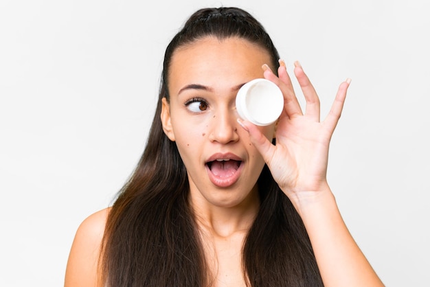 Young Arabian woman over isolated white background with moisturizer and surprised